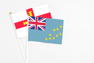 Fototapeta premium Tuvalu and Guernsey stick flags on white background. High quality fabric, miniature national flag. Peaceful global concept.White floor for copy space.