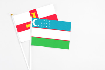 Fototapeta na wymiar Uzbekistan and Guernsey stick flags on white background. High quality fabric, miniature national flag. Peaceful global concept.White floor for copy space.