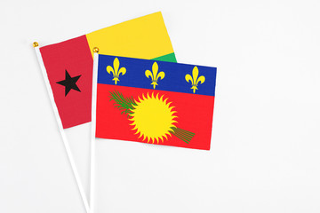 Guadeloupe and Guinea Bissau stick flags on white background. High quality fabric, miniature national flag. Peaceful global concept.White floor for copy space.