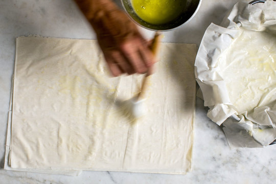 Hand spreading melt butter on filo pastry