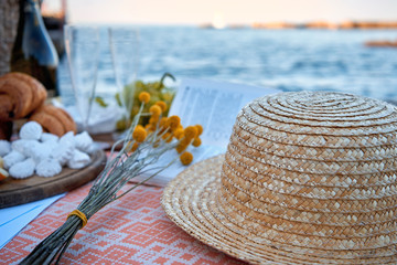 Fototapeta na wymiar Picnic by the sea. Champagne, flowers, book and tasty food, hat