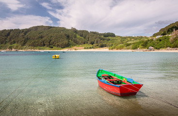 Barcas de color rojo y amarillo amarradas en un puerto natural en el oceano Atlántico, en Galicia, España.