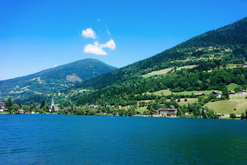 Fototapeta na wymiar Panorama of lake Field am See in Carinthia in Austria. Landscape with pond and blue sky in spring or summer. Scenery in green Alps of Europe. Countryside with Alpine mountains. Nature with water