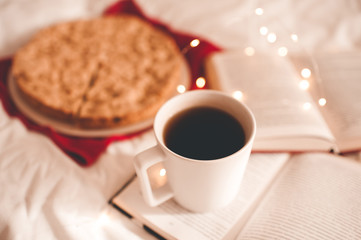 Cup of black tea on open book with apple pie at background in bed. Good morning.