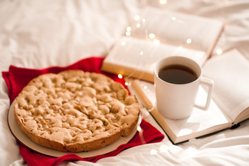 Apple pie with cup of coffee on open books in bed. Good morning. Breakfast.