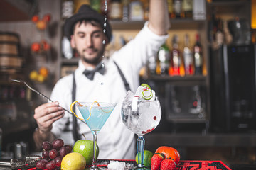 Expert barman making cocktail at night club.with hat and bow tie. Drops falling in the cup.