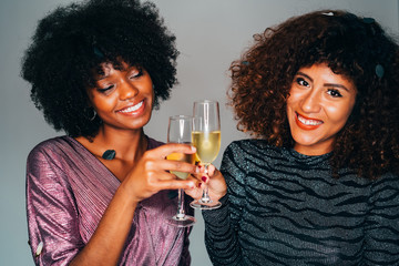 Two Young Beautiful African American women holding a glass of champagne and toasting. Cheers!