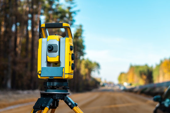 Surveyors equipment (theodolite or total positioning station) on the construction site of the road or building with construction machinery background