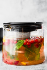 Glass teapot of cranberry, orange and mint or yellow tea isolated on bright marble background. Overhead view, copy space. Advertising for cafe menu. Coffee shop menu. Vertical photo.