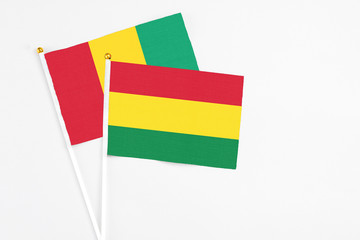 Bolivia and Guinea stick flags on white background. High quality fabric, miniature national flag. Peaceful global concept.White floor for copy space.