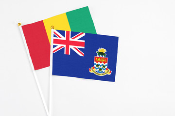 Fototapeta premium Cayman Islands and Guinea stick flags on white background. High quality fabric, miniature national flag. Peaceful global concept.White floor for copy space.