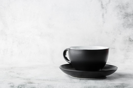 Black cup isolated on a white marble background. Horizontal photo. Tableware shop. Dishes shop. Advertising for dishware shop.
