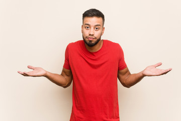 Fototapeta premium Young south-asian man doubting and shrugging shoulders in questioning gesture.