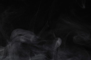 Puffs of white, gray smoke spread on a black background, curling in a fancy dance.