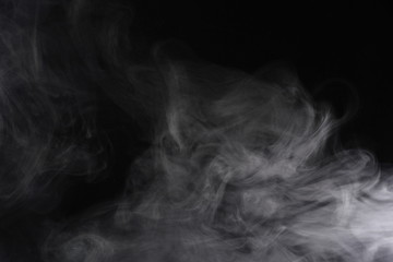 Puffs of white, gray smoke spread on a black background, curling in a fancy dance.