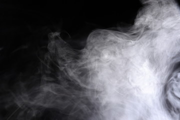 Puffs of white, gray smoke spread on a black background, curling in a fancy dance.