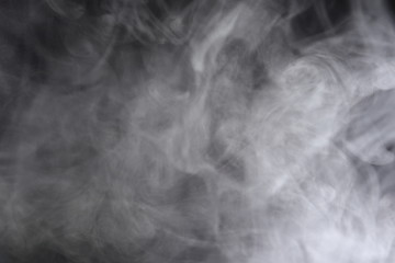 Puffs of white, gray smoke spread on a black background, curling in a fancy dance.