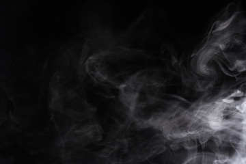 Puffs of white, gray smoke spread on a black background, curling in a fancy dance.