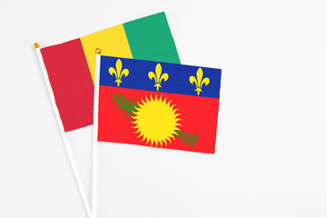 Guadeloupe and Guinea stick flags on white background. High quality fabric, miniature national flag. Peaceful global concept.White floor for copy space.