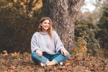 Stylish teen girl 14-16 year old wearing casual clothes posing in autumn park outdoors. Looking at camera.