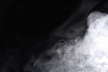 Puffs of white, gray smoke spread on a black background, curling in a fancy dance.