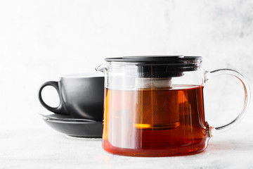 Glass teapot with dark cup of black tea isolated on bright marble background. Overhead view, copy space. Advertising for cafe menu. Coffee shop menu. Horizontal photo.