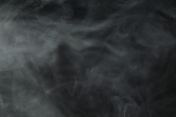 Puffs of white, gray smoke spread on a black background, curling in a fancy dance.