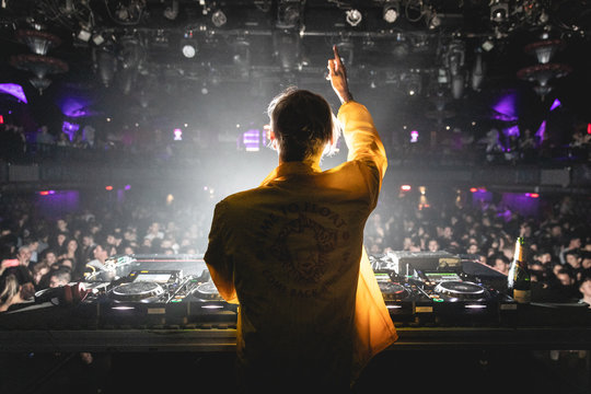 DJ With Hand Up In Yellow Jacket Facing Crowd