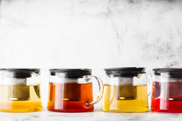 Glass teapots with four kinds of tea. Black tea, green tea isolated on bright marble background....