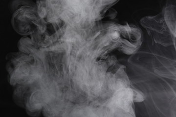 Puffs of white, gray smoke spread on a black background, curling in a fancy dance.
