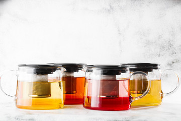 Glass teapots with four kinds of tea. Black tea, green tea isolated on bright marble background. Overhead view, copy space. Advertising for cafe menu. Coffee shop menu. Horizontal photo.