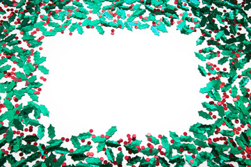 Holiday frame of sprinkles of shiny green and red holly and berries confetti with blank white copy space