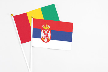 Serbia and Guinea stick flags on white background. High quality fabric, miniature national flag. Peaceful global concept.White floor for copy space.