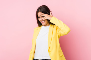 Fototapeta premium Young business woman blink at the camera through fingers, embarrassed covering face.