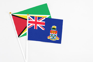 Fototapeta premium Cayman Islands and Guyana stick flags on white background. High quality fabric, miniature national flag. Peaceful global concept.White floor for copy space.