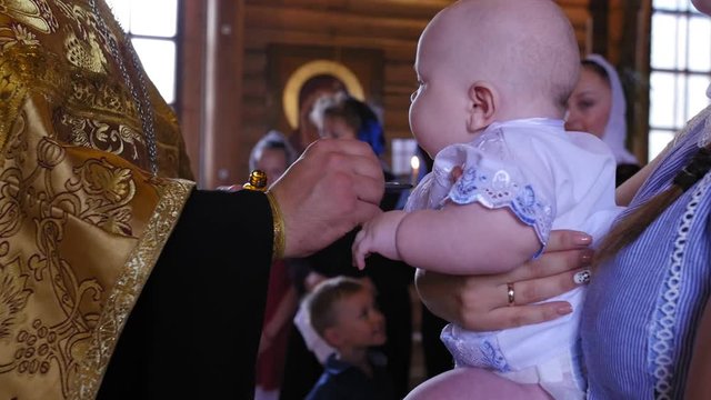 Baby boy getting babtized at a christening. Mother holds chubby baby in her arms at the ceremony of baptism in the church. Сlose up shot.