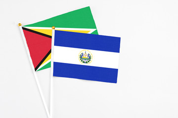 El Salvador and Guyana stick flags on white background. High quality fabric, miniature national flag. Peaceful global concept.White floor for copy space.