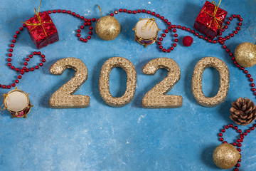 Holiday blue background with red Christmas decorations and New Year 2020 golden numbers. New Year and Christmas celebration concept. Top view. Copy space