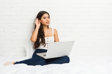 Young arab woman working with her laptop on the bed trying to listening a gossip.