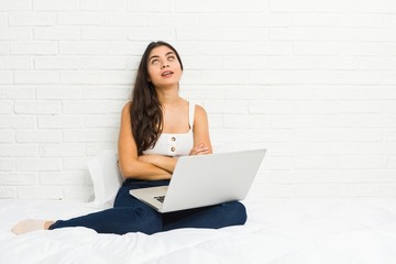 Young arab woman working with her laptop on the bed tired of a repetitive task.