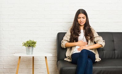 Young arab woman sitting on the sofa sick, suffering from stomachache, painful disease concept.