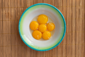 Chicken yolks lie in a white plate with a green border on a brown wooden litter