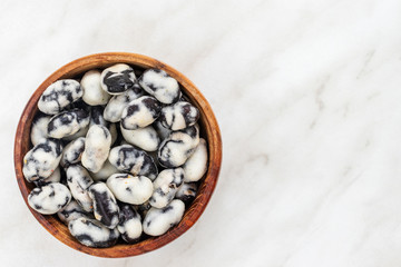 Black beans covered with salt lie in a brown bowl on a white marble surface