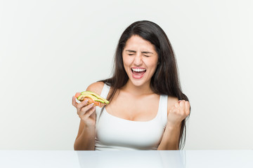 Young hispanic woman holding an avocado toast cheering carefree and excited. Victory concept.