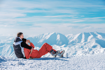Hugging couple sitting on snow and enjoying in landscape on mountain