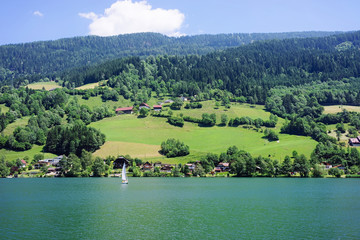 Fototapeta na wymiar Panorama of lake Field am See of Carinthia in Austria. Landscape with pond and blue sky in spring or summer. Scenery in green Alps of Europe. Countryside with Alpine mountains. Nature with water