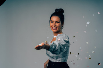 Happy Beautiful woman dressed for party playing with confetti on a white background.