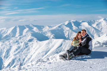 Fototapeta na wymiar Hugging couple sitting on snow and enjoying in landscape on mountain