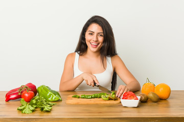 Young curvy woman preparing a healthy meal happy, smiling and cheerful.