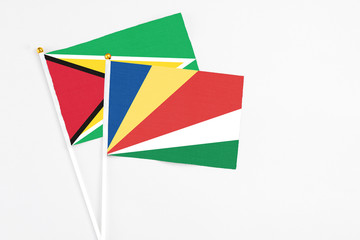 Obraz premium Seychelles and Guyana stick flags on white background. High quality fabric, miniature national flag. Peaceful global concept.White floor for copy space.